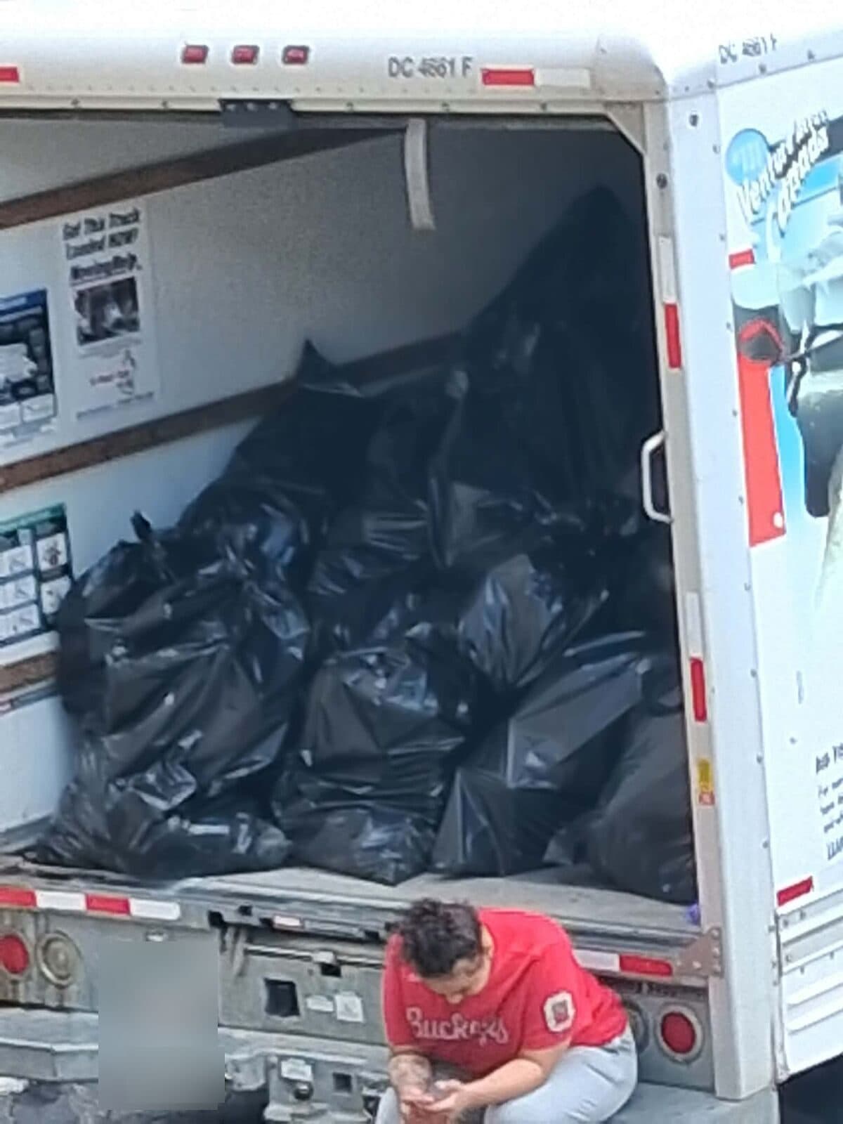Crew member beside a box truck loaded with black trash bags