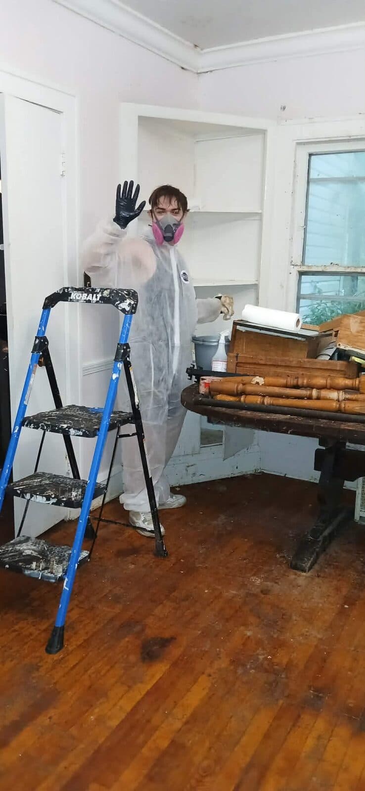 Crew member in a protective suit and pink respirator waving beside a step ladder