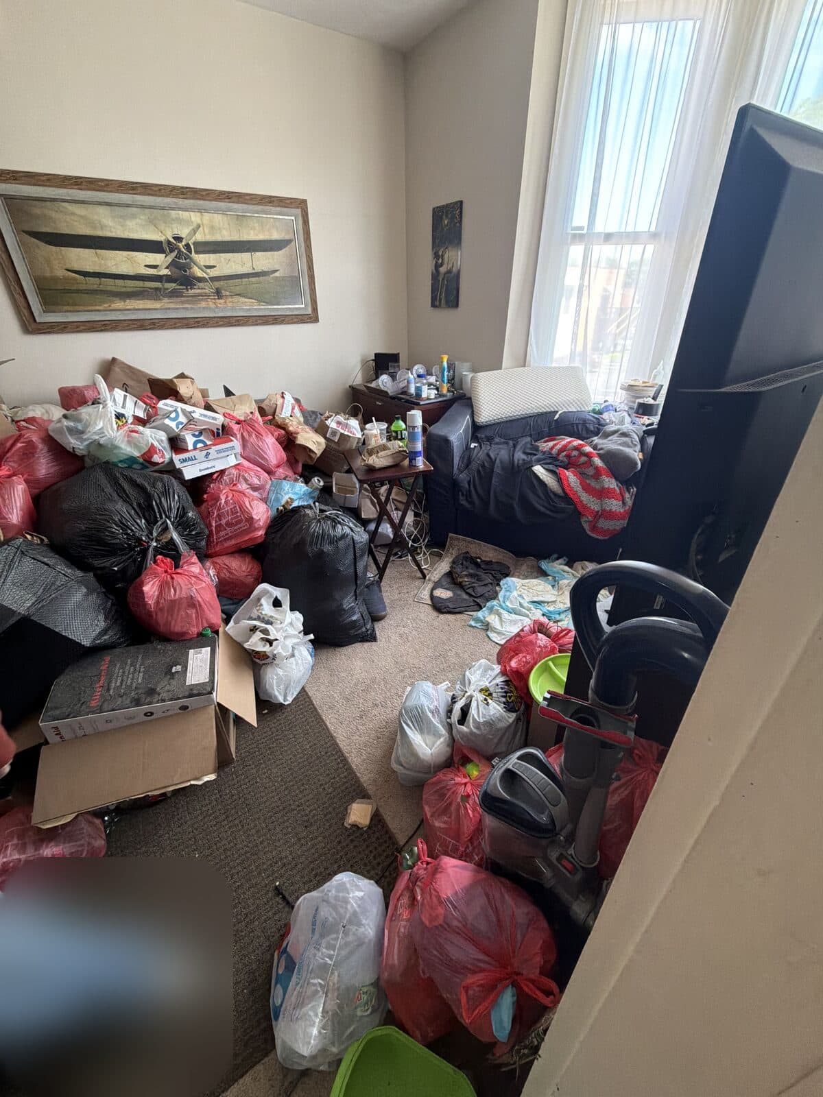 Before: Apartment living room filled with piled trash bags and boxes