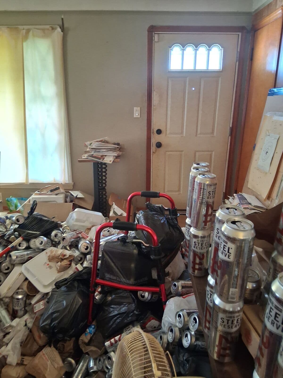 Before: Living area by the front door piled with cans and bags