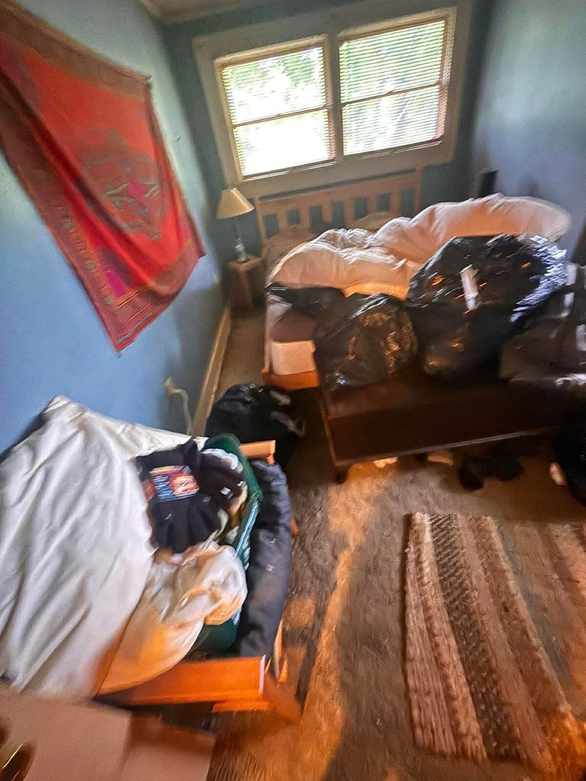 Before: Bedroom with bed and floor covered in bags and belongings